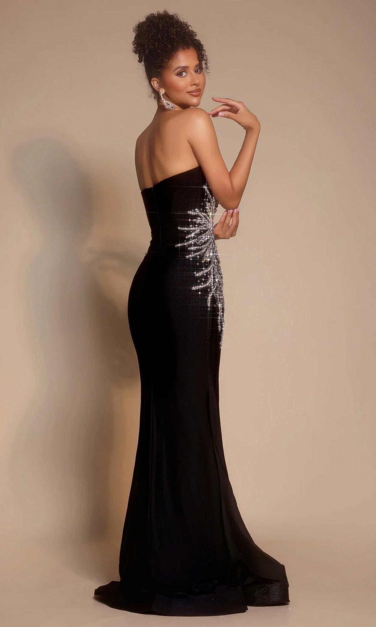 A woman poses against a plain beige background wearing the Portia and Scarlett PS26331E long formal dress, featuring a strapless sweetheart neckline and silver sequin detailing on the side.